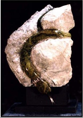 The work V/7 is a small sculpture from serpentine with a pedestal from slate. It shows a white stone around which a small green snake writhes itself.